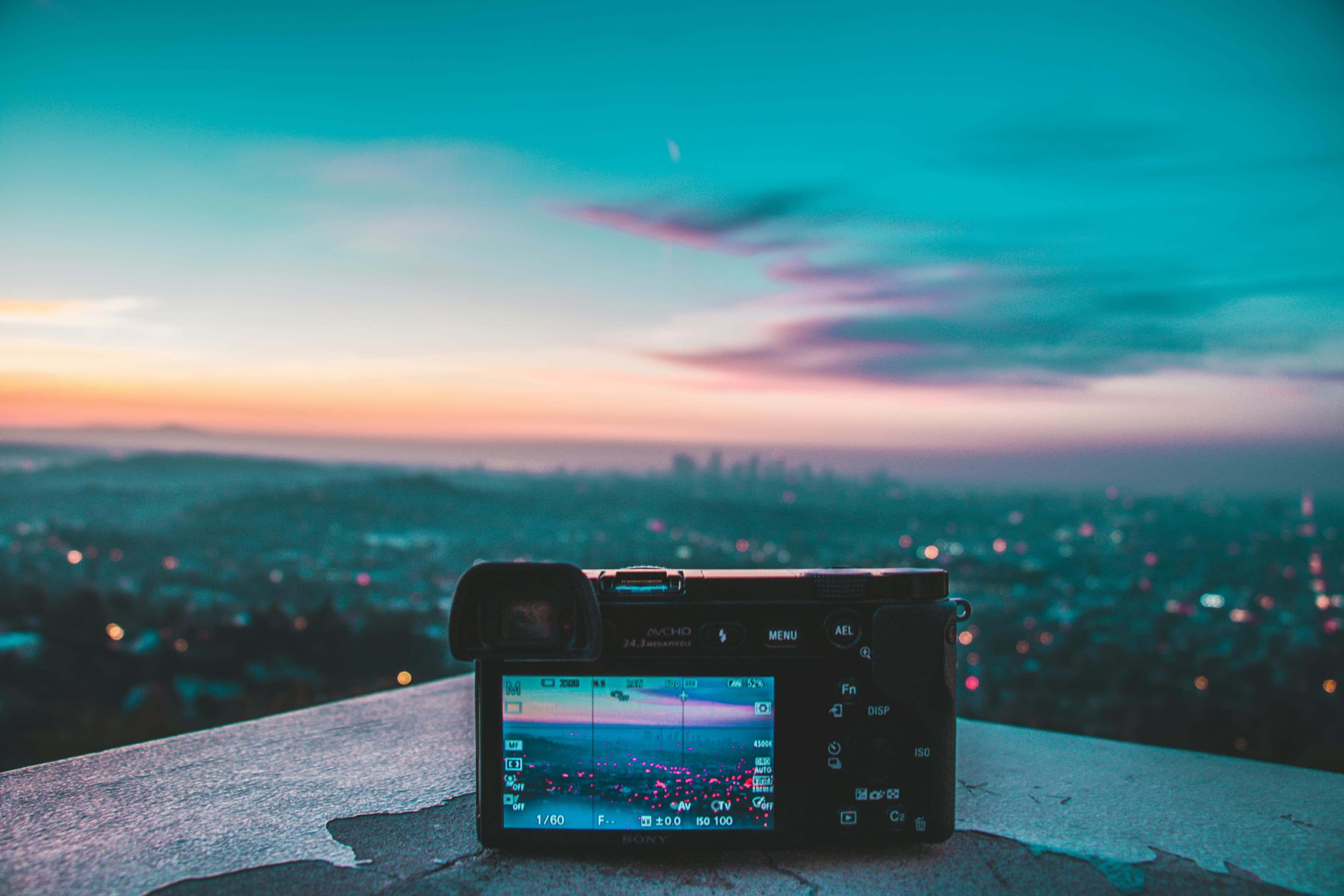 A digital camera placed on a ledge, capturing a cityscape at sunset.
